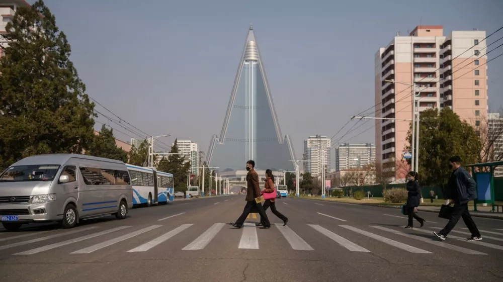 People wearing face masks walk across a street before the Ryugyong hotel (back C) on the occasion of the 108th birthday of late North Korean leader Kim Il Sung, known as the 'Day of the Sun', in Pyongyang on April 15, 2020.,Image: 513917283, License: Rights-managed, Restrictions:, Model Release: no