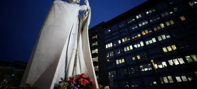 A statue of the late Pope John Paul II stands surrounded by candles and flowers outside the Gemelli Hospital where Pope Francis has gone to continue treatment for ongoing bronchitis, in Rome, Italy, February 17, 2025. REUTERS/Guglielmo Mangiapane   TPX IMAGES OF THE DAY