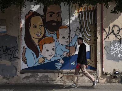 A man walks his dog past graffiti of Shiri and Yarden Bibas and their sons, Ariel, left, and Kfir, right, who were taken captive by Hamas, in Tel Aviv, Israel, Wednesday, Feb. 19, 2025. Yarden Bibas was freed from captivity earlier this month. (AP Photo/Oded Balilty)