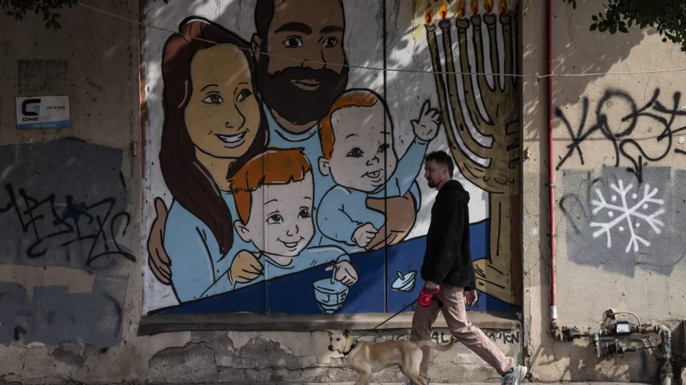 A man walks his dog past graffiti of Shiri and Yarden Bibas and their sons, Ariel, left, and Kfir, right, who were taken captive by Hamas, in Tel Aviv, Israel, Wednesday, Feb. 19, 2025. Yarden Bibas was freed from captivity earlier this month. (AP Photo/Oded Balilty)