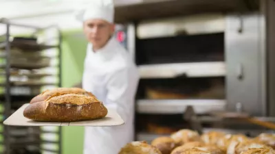 Baker of small bakery holding hot bread on shovel just from oven, showing good quality of product / Foto: Jackf