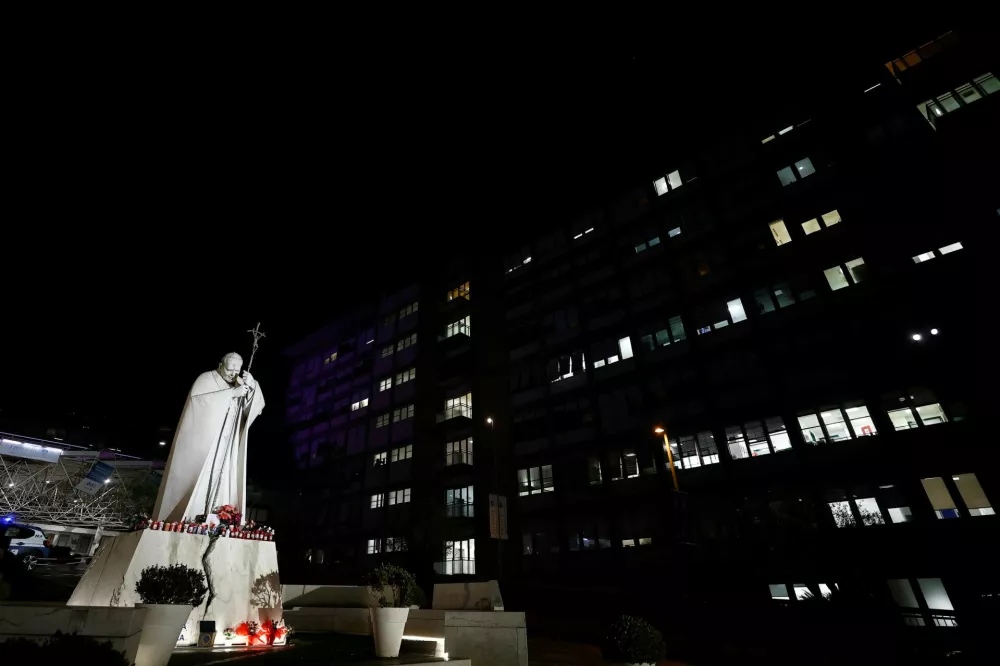 Decorated candles, flowers, and pictures of Pope Francis are placed at the base of the statue of the late Pope John Paul II outside Gemelli Hospital, where Pope Francis is admitted for treatment, in Rome, Italy, February 22, 2025. REUTERS/Vincenzo Livieri