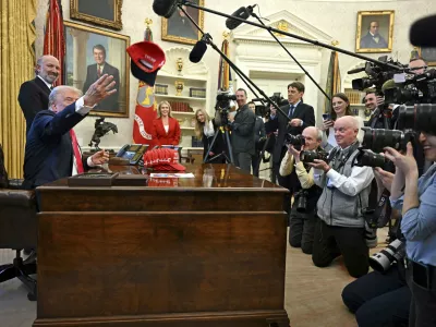 President Donald Trump throws a hat that reads "Trump Was Right About Everything" as he talks to reporters while Commerce Secretary Howard Lutnick, and White House press secretary Karoline Leavitt, back center, watch, in the Oval Office at the White House in Washington, Tuesday, Feb. 25, 2025. (Pool via AP)