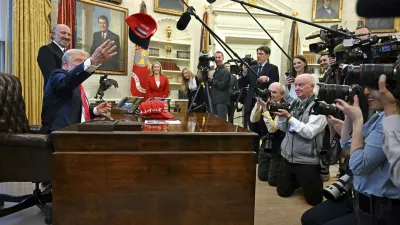 President Donald Trump throws a hat that reads "Trump Was Right About Everything" as he talks to reporters while Commerce Secretary Howard Lutnick, and White House press secretary Karoline Leavitt, back center, watch, in the Oval Office at the White House in Washington, Tuesday, Feb. 25, 2025. (Pool via AP)