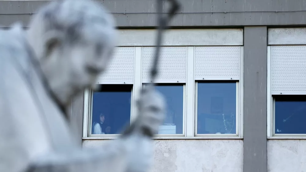 People are seen near a window as the statue of late Pope John Paul II stands outside Gemelli Hospital, where Pope Francis is admitted for treatment, in Rome, Italy, February 27, 2025. REUTERS/Yara Nardi