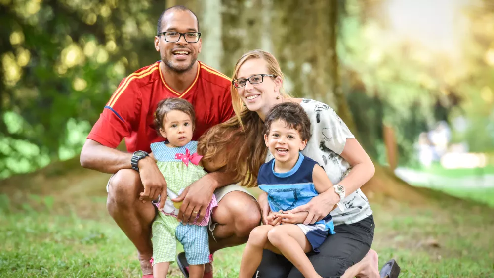 Happy interracial family is enjoying a day in the park. Little mulatto baby girl and boy. Successful adoption. Diverse family in nature with sun in the back.