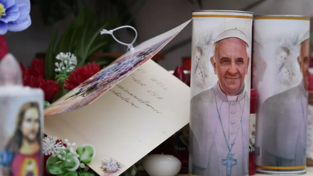 Candles with the pictures of Pope Francis are the laid under the statue of late Pope John Paul II outside Agostino Gemelli Polyclinic in Rome, Wednesday, Feb. 19, 2025, where the Pontiff is hospitalized since Friday, Feb. 14. (AP Photo/Gregorio Borgia)