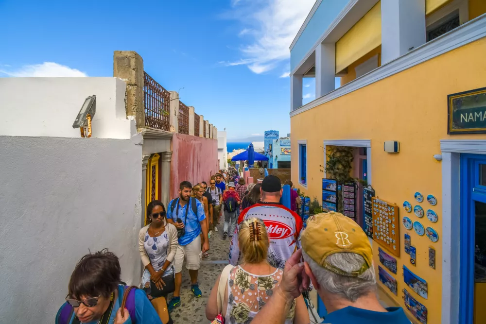 The effects of overtourism as tourists crowd the narrow streets through the Greek Isle resort of Oia and Fira on the island of Santorini, Greece. Santorini is one of the Cyclades islands in the Aegean Sea. It was devastated by a volcanic eruption in the 16th century BC, forever shaping its rugged landscape. The whitewashed, cubiform houses of its 2 principal towns, Fira and Oia, cling to cliffs above an underwater caldera crater.