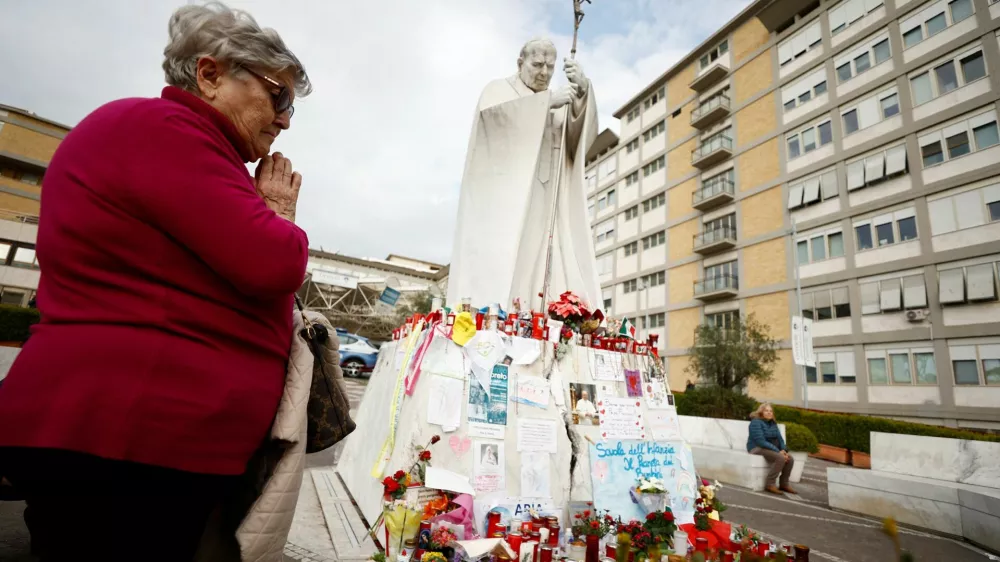 A woman prays near the statue of late Pope John Paul II outside Gemelli Hospital, where Pope Francis is admitted for treatment, in Rome, Italy, March 8, 2025. REUTERS/Vincenzo Livieri