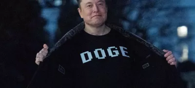 Elon Musk flashes his t-shirt that reads "DOGE" to the media as he walks on South Lawn of the White House, in Washington, Sunday, March 9, 2025. (AP Photo/Jose Luis Magana)