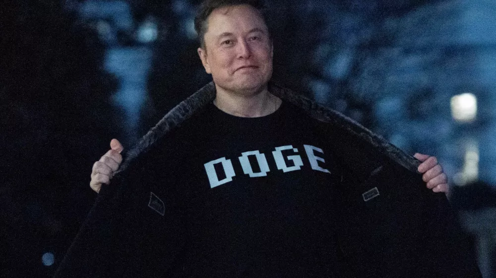 Elon Musk flashes his t-shirt that reads "DOGE" to the media as he walks on South Lawn of the White House, in Washington, Sunday, March 9, 2025. (AP Photo/Jose Luis Magana)