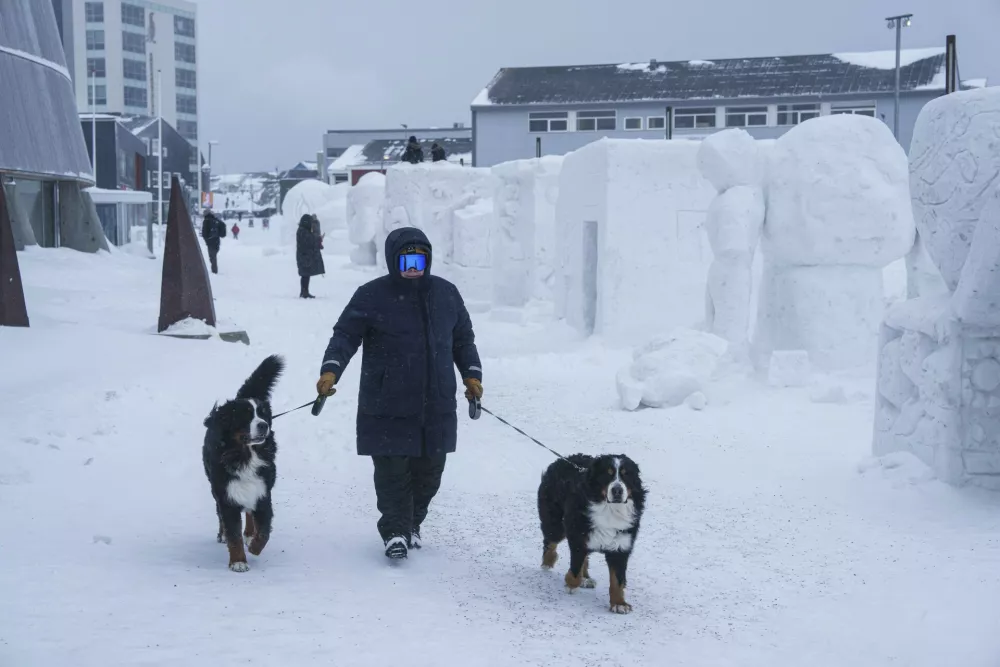 A man walks with his dogs on pedestrian street past snow sculptures in Nuuk, Greenland, Saturday, March 8, 2025. (AP Photo/Evgeniy Maloletka)