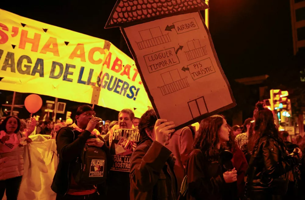 FILE PHOTO: A demonstrator holds a house-shaped sign that reads "from touristic flat to temporary rent to Airbnb" during a protest to demand lower housing rental prices and better living conditions, in Barcelona, Spain, November 23, 2024. REUTERS/Bruna Casas/File Photo / Foto: Bruna Casas