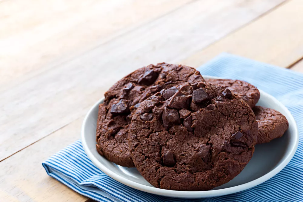 Soft baked dark chocolate cookies in white plate on blue stripes napkin, Close up image / Foto: Chatri Attanatwong