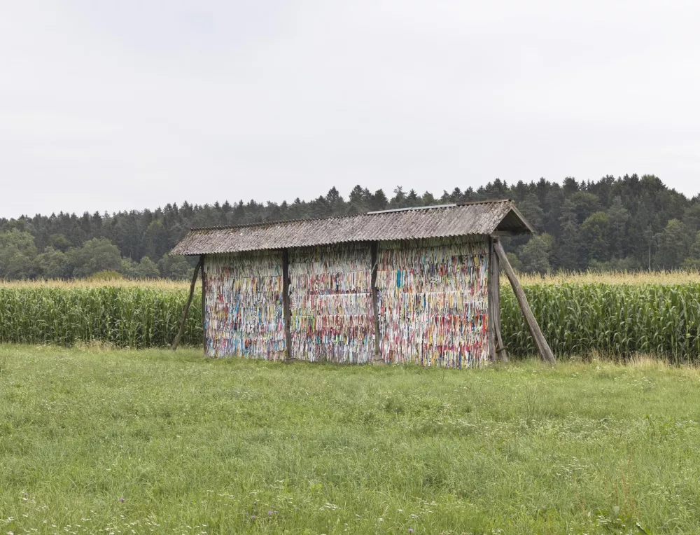 DNLM: Iz serije Preglaševanje jesiharja, 2023, kozolec z barvnimi trakovi: intervencija v kozolec z razrezanimi reklamnimi ponjavami. Foto: Jaka Babnik
