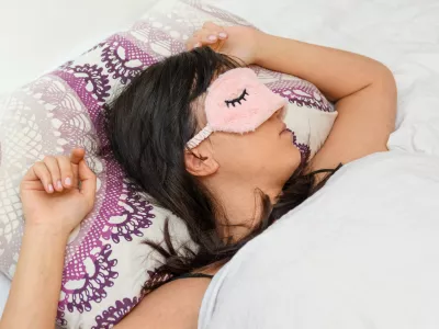 A shallow focus closeup of a female wearing a sleeping eye cover while lying on the bed / Foto: Wirestock