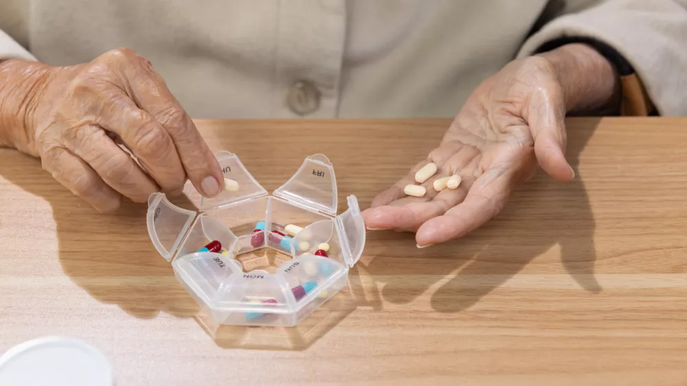 Elderly woman putting pills into pill box for the week. / Foto: Toa55