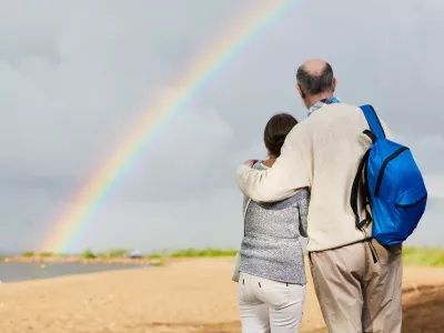 Affectionate aged couple looking at rainbow against grey cloudy sky / Foto: Shironosov
