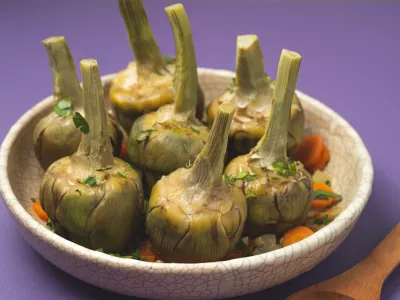 French artichokes à la Barigoule or Carciofi alla provenzal. Provencal artichokes stewed with carrots, onions, white wine, bay leaves and Provençal herbs. Spring recipes from southern France. Lavender background / Foto: Uliu