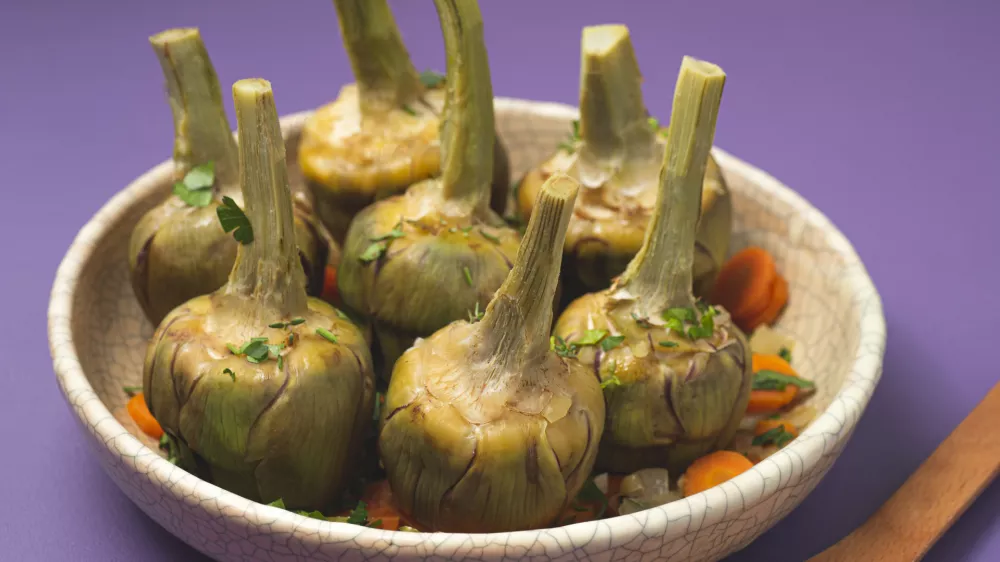 French artichokes à la Barigoule or Carciofi alla provenzal. Provencal artichokes stewed with carrots, onions, white wine, bay leaves and Provençal herbs. Spring recipes from southern France. Lavender background / Foto: Uliu