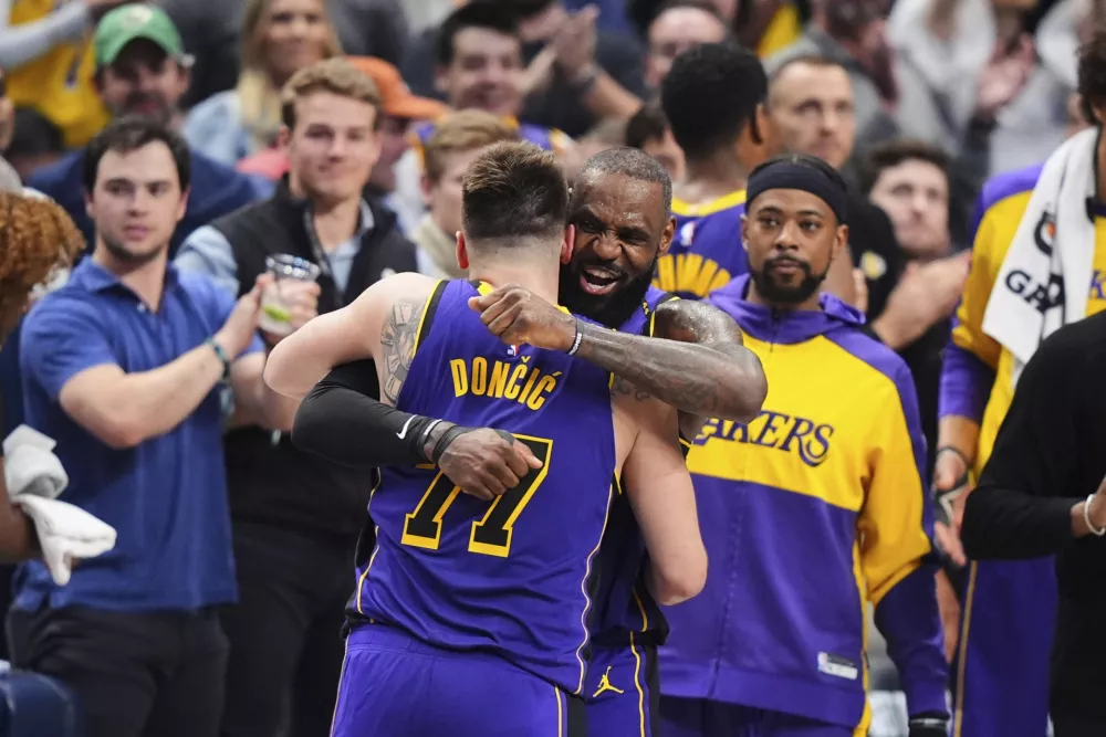 Los Angeles Lakers' Luka Doncic (77) and LeBron James, center, right, hug and celebrate late in the second half of an NBA basketball game against the Dallas Mavericks in Dallas, Wednesday, April 9, 2025. (AP Photo/LM Otero)