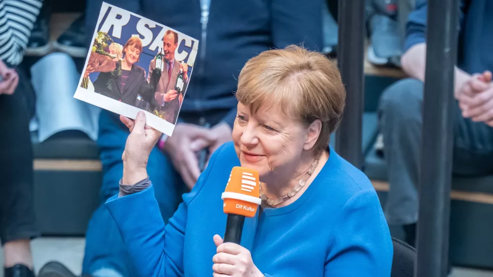 10 April 2025, Berlin: Former German Chancellor Angela Merkel holds a picture of her and Friedrich Merz as she speaks during her appearance as a guest on Deutschlandfunk's live radio show "Studio 9" at the Humboldt Forum. Photo: Michael Kappeler/dpa