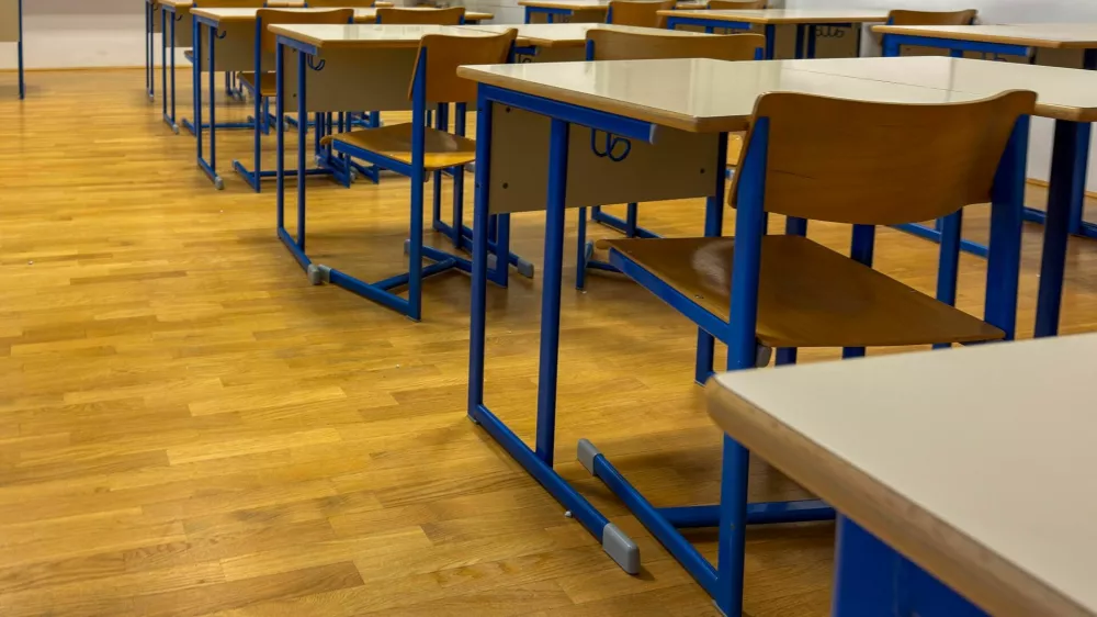 Modern, well-lit classroom with rows of empty wooden desks and blue-framed chairs on a polished wooden floor. The organized, quiet setting evokes themes of education, back to school, academic preparation, and the learning environment. Perfect for content related to schools, teaching, or educational systems. / Foto: Bamm-bamm