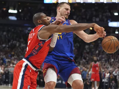 Los Angeles Clippers guard Kris Dunn, left, fouls Denver Nuggets center Nikola Jokic, right, as they pursue the ball in overtime of Game 1 of an NBA first-round playoff series Saturday, April 19, 2025, in Denver. (AP Photo/David Zalubowski)