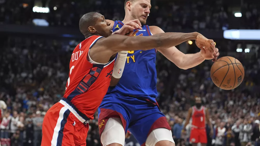Los Angeles Clippers guard Kris Dunn, left, fouls Denver Nuggets center Nikola Jokic, right, as they pursue the ball in overtime of Game 1 of an NBA first-round playoff series Saturday, April 19, 2025, in Denver. (AP Photo/David Zalubowski)
