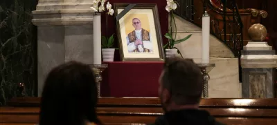 A couple sits near a portrait of Pope Francis, following his death, in the Catholic Cathedral of Saint Dionysius the Areopagite, in Athens, Greece, April 22, 2025. REUTERS/Louisa Gouliamaki