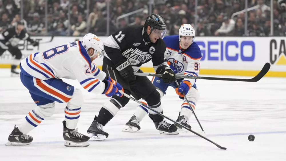 Los Angeles Kings center Anze Kopitar, center, moves the puck while under pressure from Edmonton Oilers right wing Connor Brown, left, and center Ryan Nugent-Hopkins during the second period in Game 1 of an NHL hockey first-round playoff series Monday, April 21, 2025, in Los Angeles. (AP Photo/Mark J. Terrill)