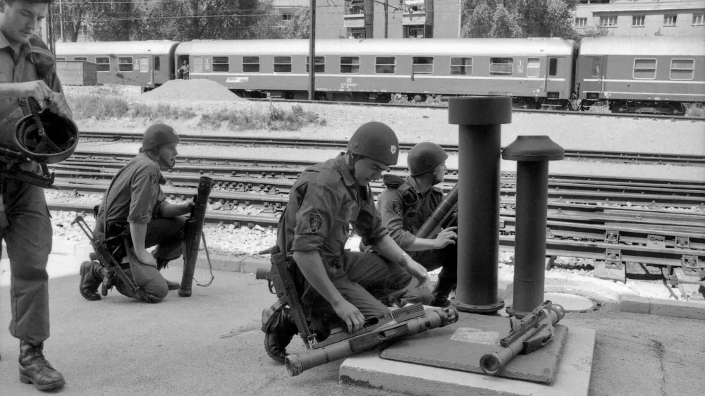 ﻿Pripadniki specialne enote milice med napovedjo letalskega napada na železniški postaji na Jesenicah 2. julija 1991. 