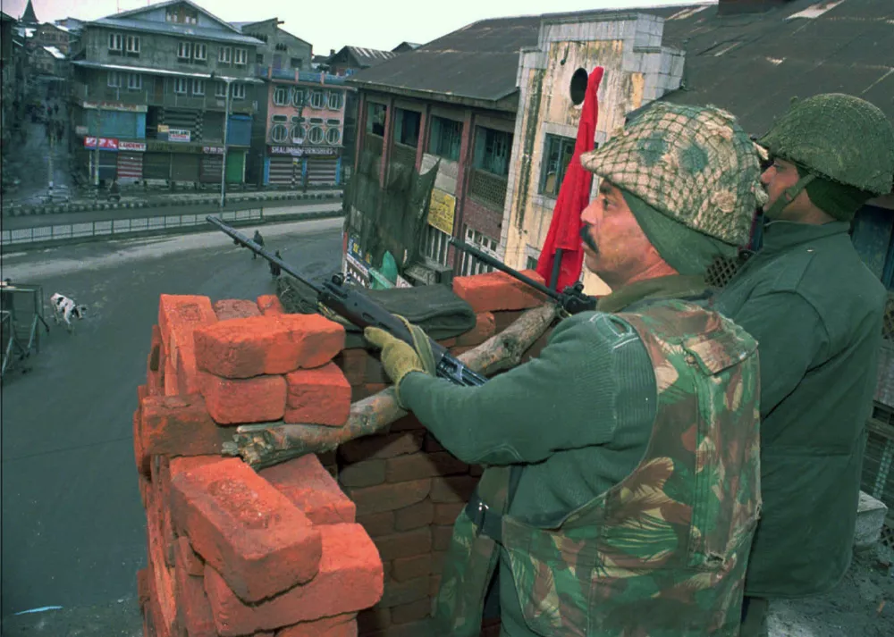Indian paramilitary troops stand guard at their roof-top vantage point on a building above the deserted streets during a high alert in central Srinagar Tuesday January 25, 2000. Security has been beefed up in the troubled area after militants attacked an army camp in Srinagar, kiiling two officers and wounding eight. Two militants were also killed in the gunbattle. (AP Photo/Rafiq Maqbool)