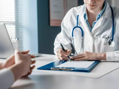 Doctor sitting at desk and writing a prescription for her patient / Foto: Demaerre