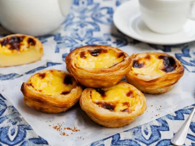 Egg tart, traditional Portuguese dessert, pastel de nata on a parchment paper. Blue background / Foto: Annapustynnikova