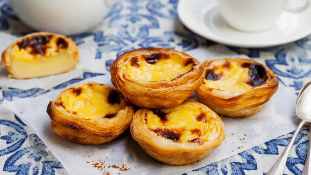 Egg tart, traditional Portuguese dessert, pastel de nata on a parchment paper. Blue background / Foto: Annapustynnikova