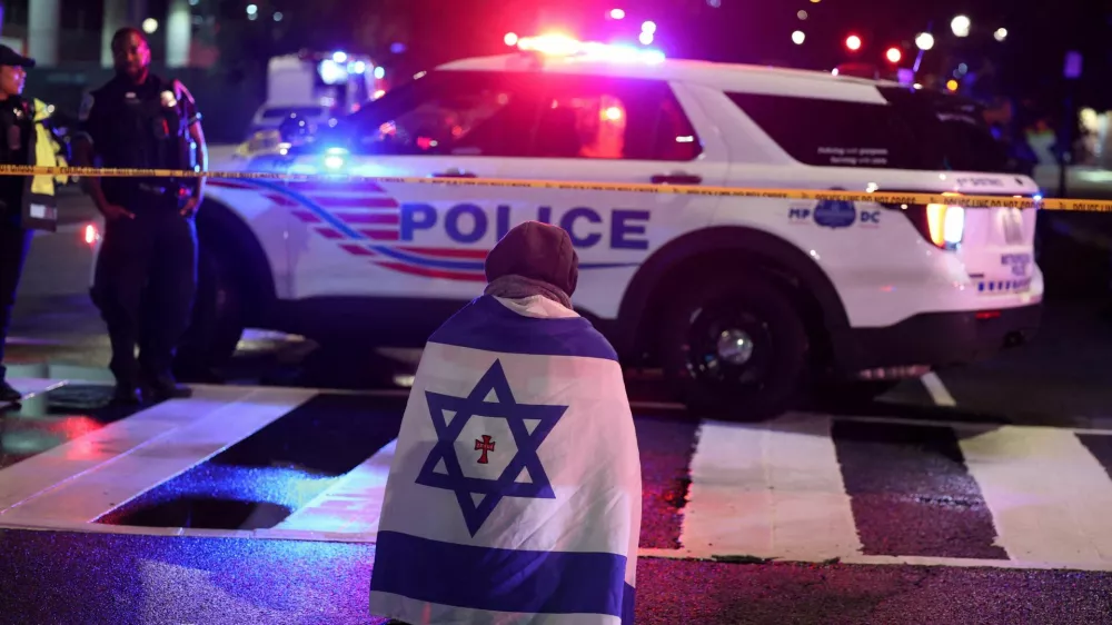 A man, with an Israeli flag with a cross in the center, kneels next to emergency personnel working at the site where, according to the U.S. Homeland Security Secretary, two Israeli embassy staff were shot dead near the Capital Jewish Museum in Washington, D.C., U.S. May 21, 2025. REUTERS/Jonathan Ernst  TPX IMAGES OF THE DAY