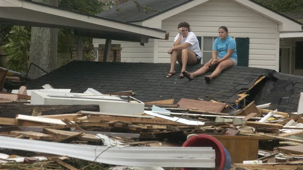 Melanie Seaman, left, and her daughter Miranda sit on the detached roof of a relatives home on Washington Avenue in Pascagoula, Miss., on Monday, Aug. 29, 2005, after Hurricane Katrina made landfall causing severe damage to the area. (AP Photo/Mississippi Press, William Colgin)