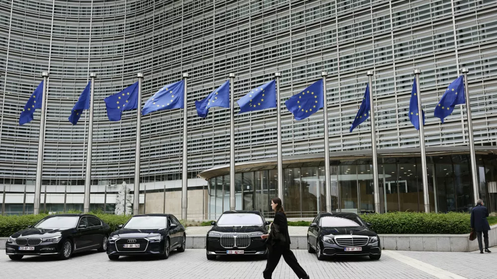 European Union flags flap in the wind as a woman walks past diplomatic vehicles outside of EU headquarters in Brussels, Belgium, Tuesday, May 27, 2025. (AP Photo/Omar Havana)