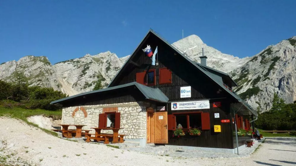 Poštarski dom na Vršiču ima med vsemi vršiškimi postojankami najlepši razgled; na vzpetini pred domom je razgledna plošča z označenimi vrhovi, ki se vidijo. F Kranjska gora