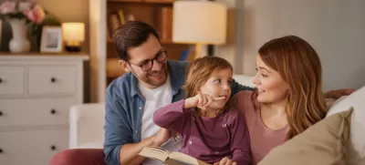 Family with little daughter reading book on sofa in living room