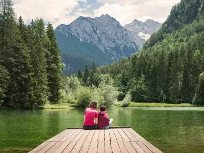 Mother sitting on the dock hugging her son, enjoying the majestic mountain and lake view. Family time and vacation concepts. / Foto: 24k-production