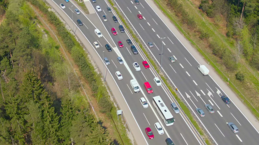 DRONE: Flying above cars moving along entry lane during a traffic jam on the highway. Crowd of commuters and tourists on their way to summer holiday destination get stuck in a congestion on freeway.