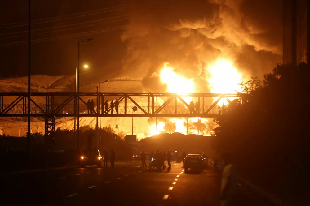 People watch from a bridge as flames from an Israeli attack rise from Sharan Oil depot, following Israeli strikes on Iran, in Tehran, Iran, June 15, 2025. Majid Asgaripour/WANA (West Asia News Agency) via REUTERS  ATTENTION EDITORS - THIS PICTURE WAS PROVIDED BY A THIRD PARTY