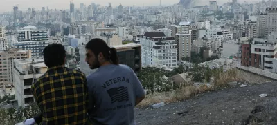 A man wears a U.S. veteran-themed shirt, that reads, "United we stand", as smoke rises in the distance, following an Israeli attack on the IRIB building, the country's state broadcaster, in Tehran, Iran, June 16, 2025. Majid Asgaripour/WANA (West Asia News Agency) via REUTERS  ATTENTION EDITORS - THIS PICTURE WAS PROVIDED BY A THIRD PARTY. TPX IMAGES OF THE DAY.