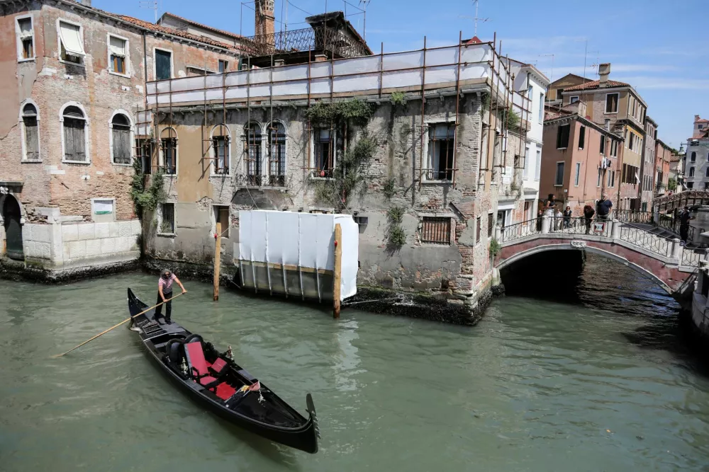 A man rows on a gondola near Banksy's 'Migrant Child', the mural depicting a migrant child wearing a lifejacket and holding a pink flare, as its restoration process begins, in Venice, Italy, June 17, 2025. The mural appeared on San Pantalon palace in 2019 and it will be restored by Ifis art. REUTERS/Manuel Silvestri