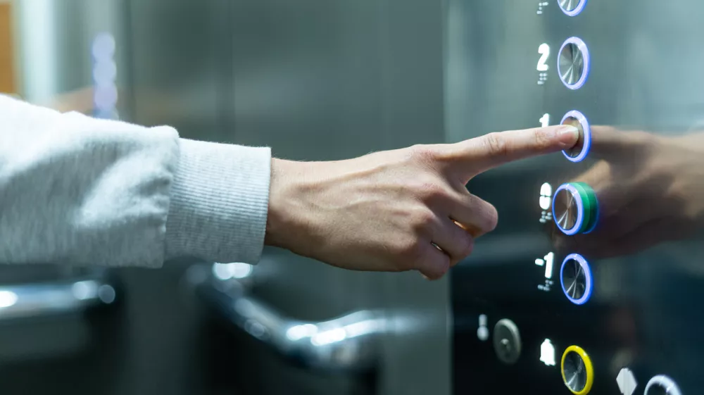 Closeup of person's hand pushing button to select first floor in elevator. Passenger lift. Businessman in office. Movement within building concept
