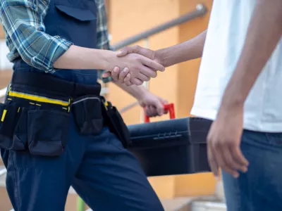 Cropped photo of a repairman holding a toolbox while shaking hands with his client outdoors / Foto: Oleksandr But