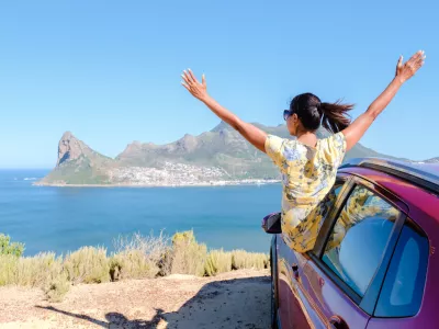 woman outside a car window with hands up, a car at Chapmans Peak Drive in Cape Town South Africa looking out over the ocean. women on a road trip garden route South Africa with renal car / Foto: Fokkebok