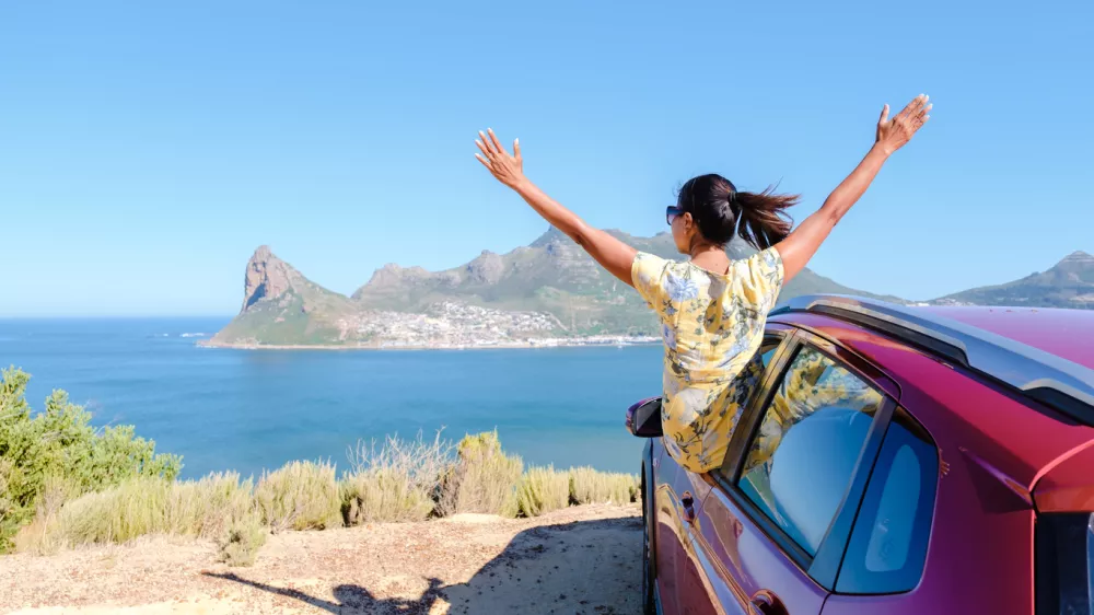 woman outside a car window with hands up, a car at Chapmans Peak Drive in Cape Town South Africa looking out over the ocean. women on a road trip garden route South Africa with renal car / Foto: Fokkebok